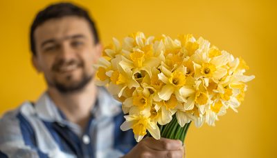 A young smiling man with a bouquet of daffodils on a colored background. The concept of greetings and women's day.