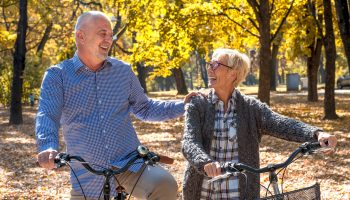 A happy elderly couple riding a bicycle in the park in the autumn